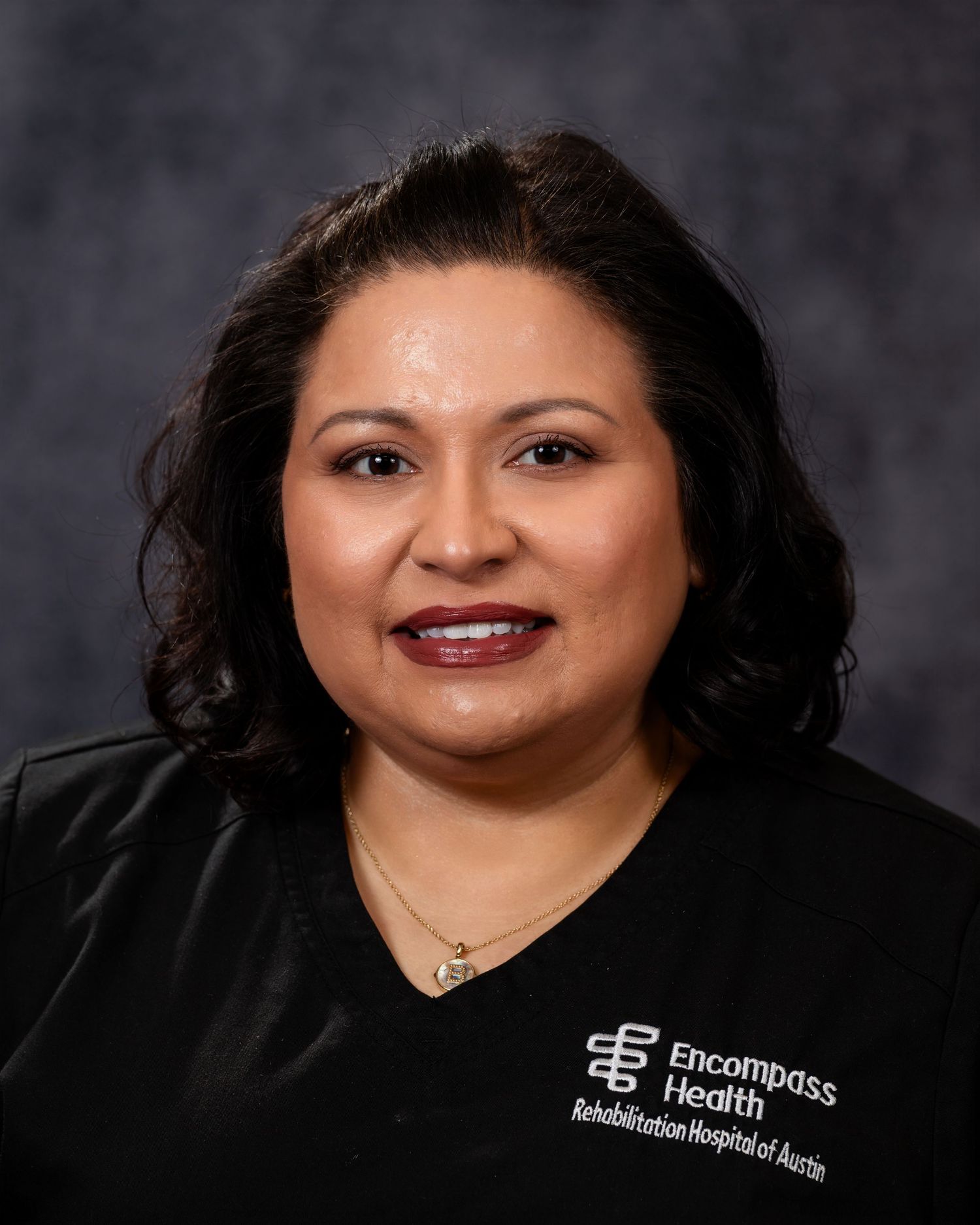 Professional headshot portrait against dark background showing warm smile and black attire.