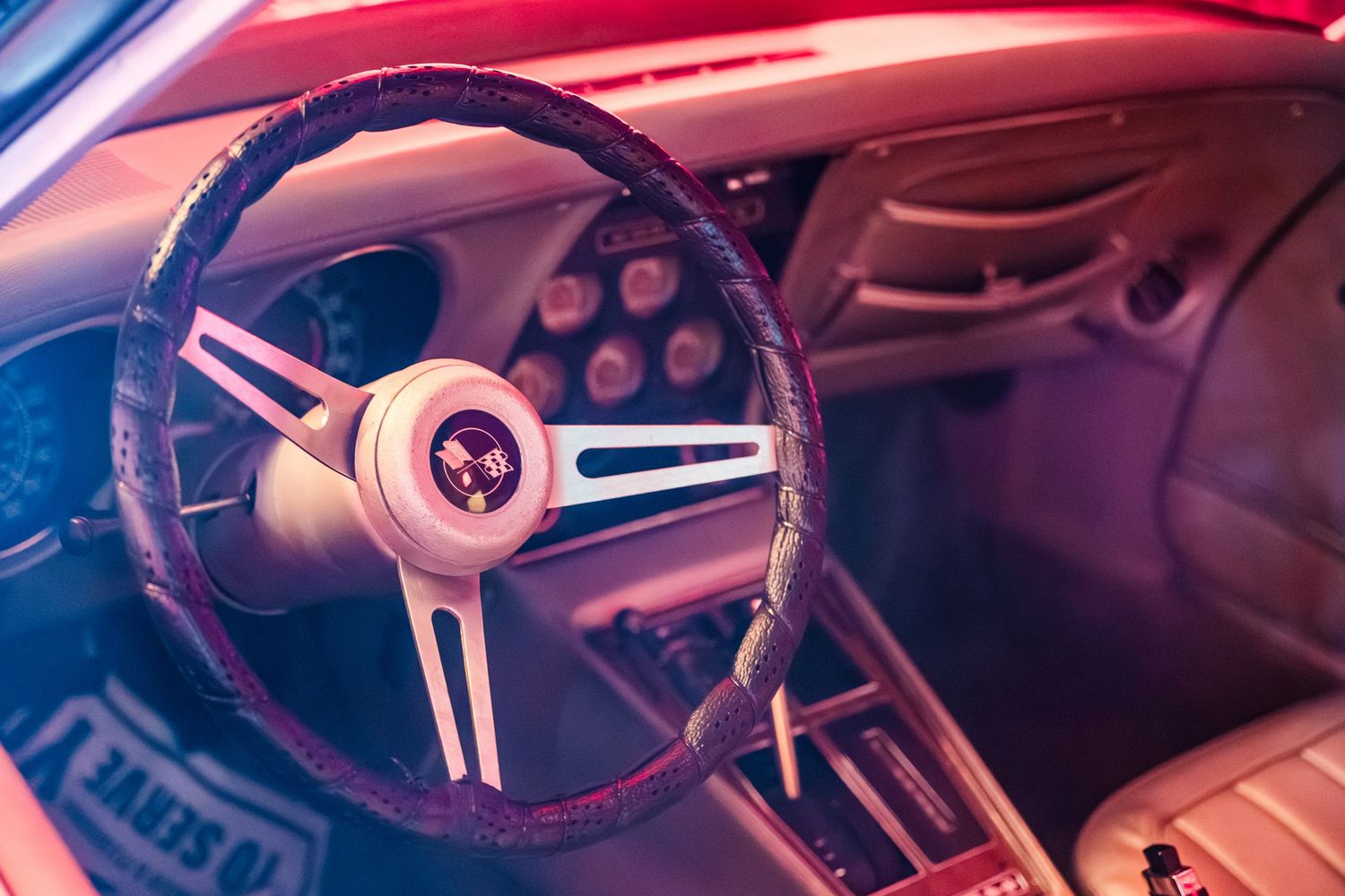 Close-up view of a car steering wheel illuminated by vibrant pink and blue neon lighting.