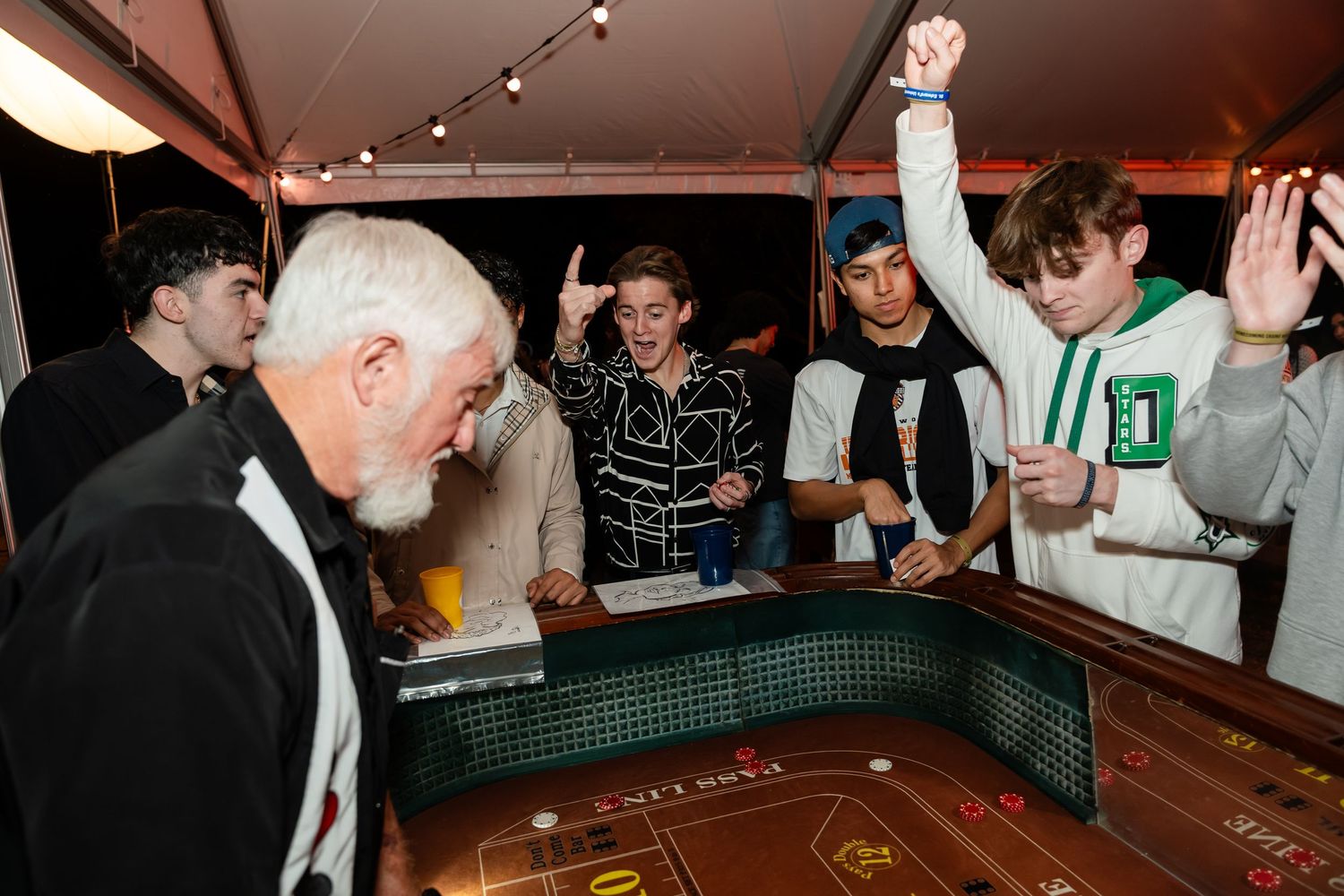 A group of people gathered around a craps table in a casino setting with overhead lighting.