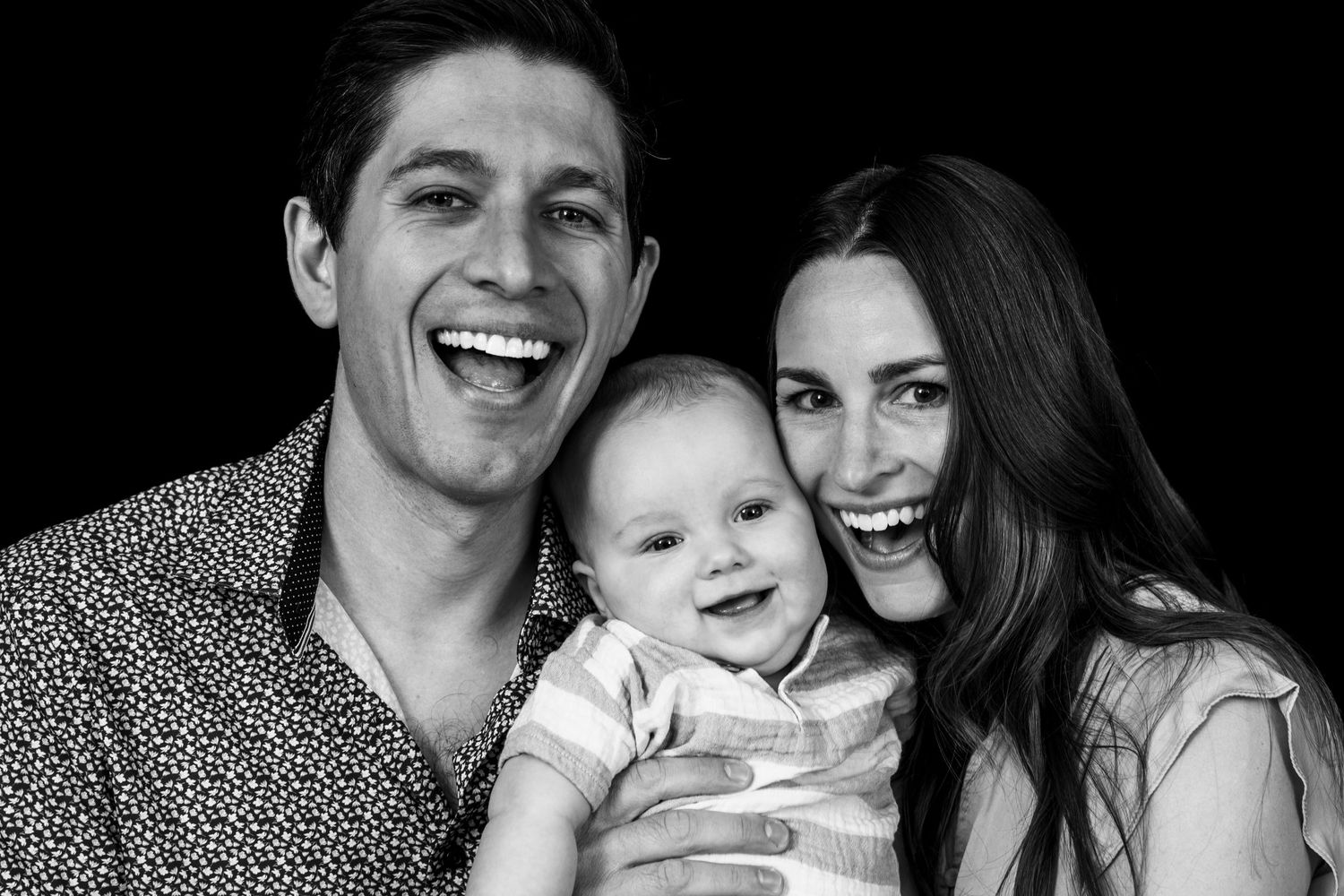 Black and white portrait of a happy family with a smiling baby wearing light colored clothing.