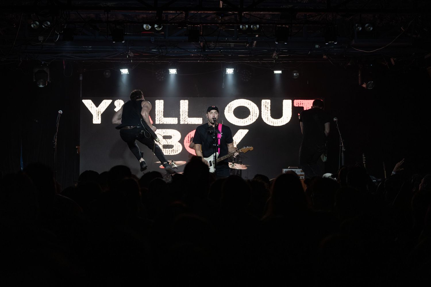 Fall Out Boy performing live on stage with dramatic lighting and bold logo backdrop at a concert venue.