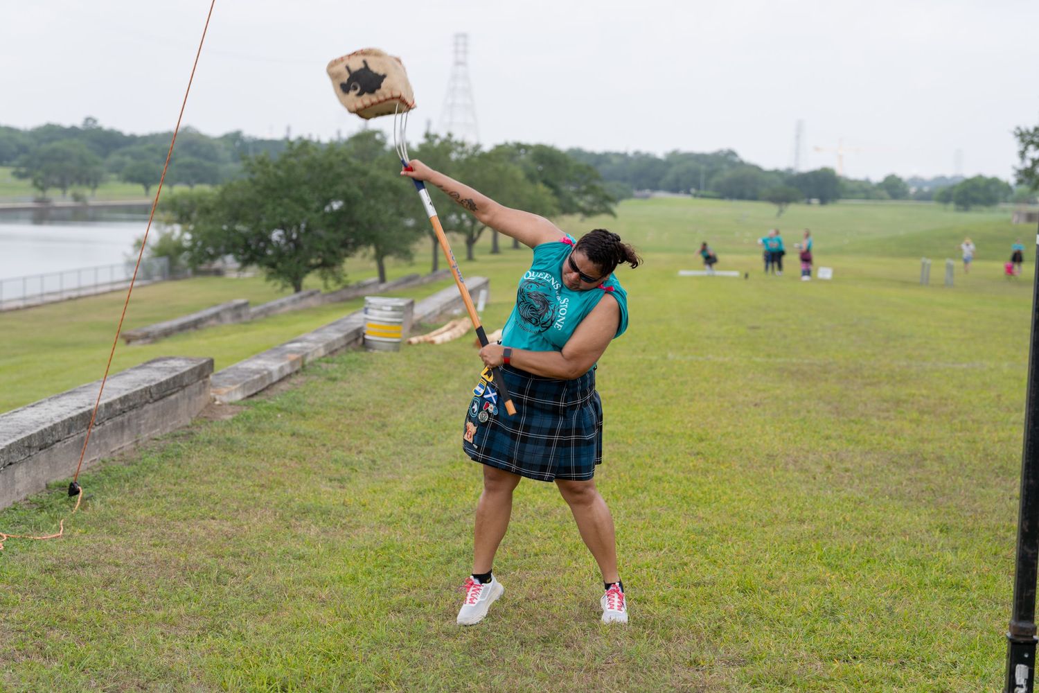 Woman in kilt throwing hammer at Highland Games competition on green field.