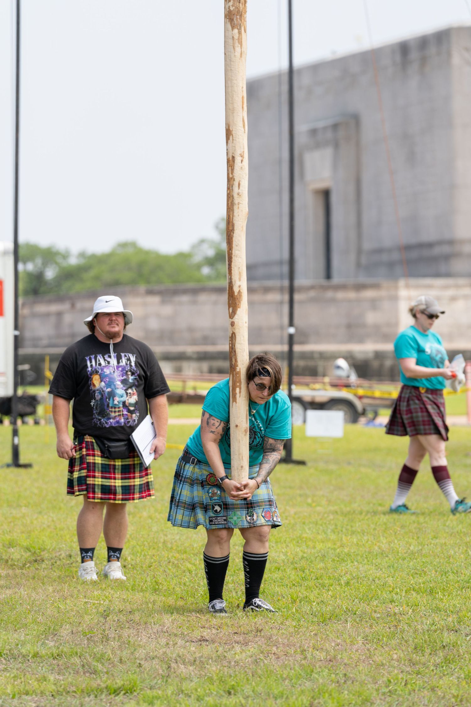 Athletes in kilts compete in caber toss at a Scottish Highland Games event on a green field.