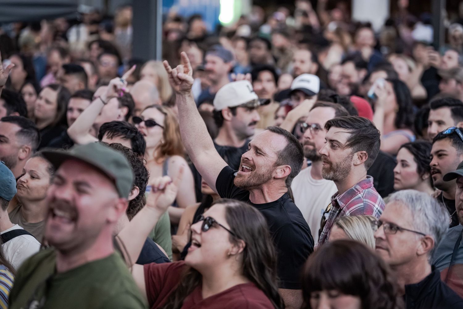 Large crowd of excited concert-goers cheering and raising hands at an outdoor music festival.