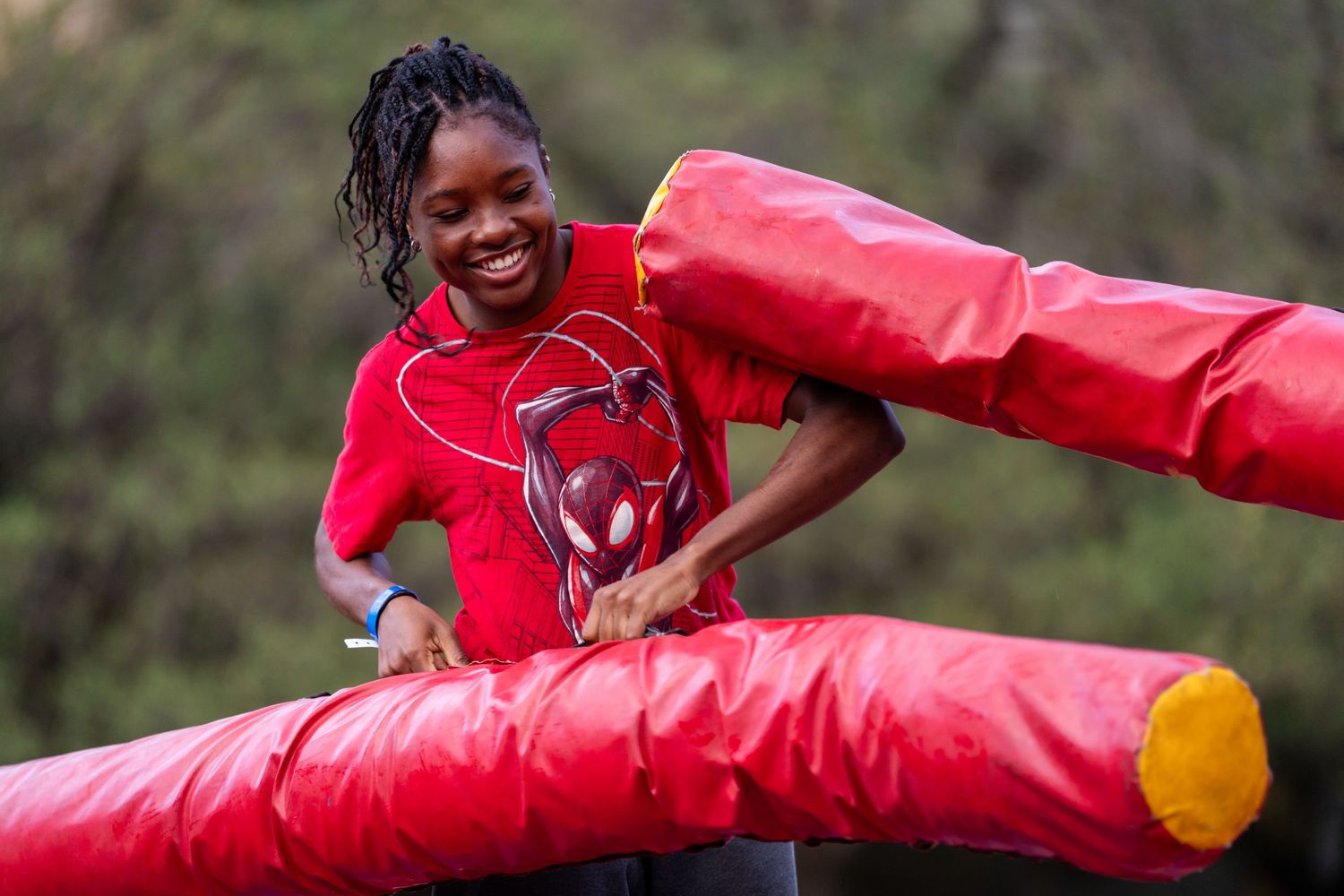 Young woman in red Spider-Man shirt navigating inflatable obstacle course outdoors.