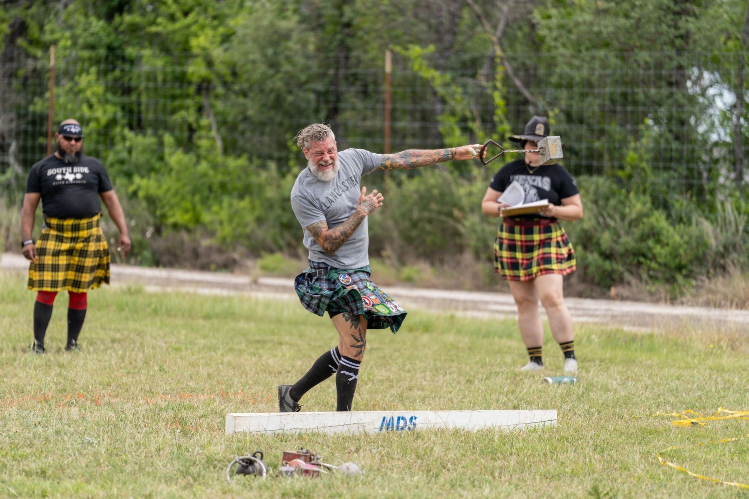 Man in kilt competes in Highland Games throwing event, with spectators watching outdoors.