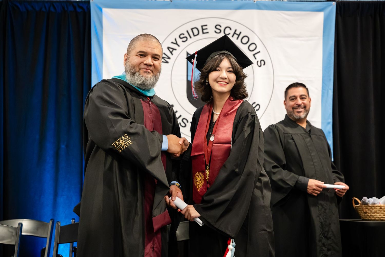 Graduate shakes hands with faculty in academic robes at Wayside Schools graduation ceremony on stage.