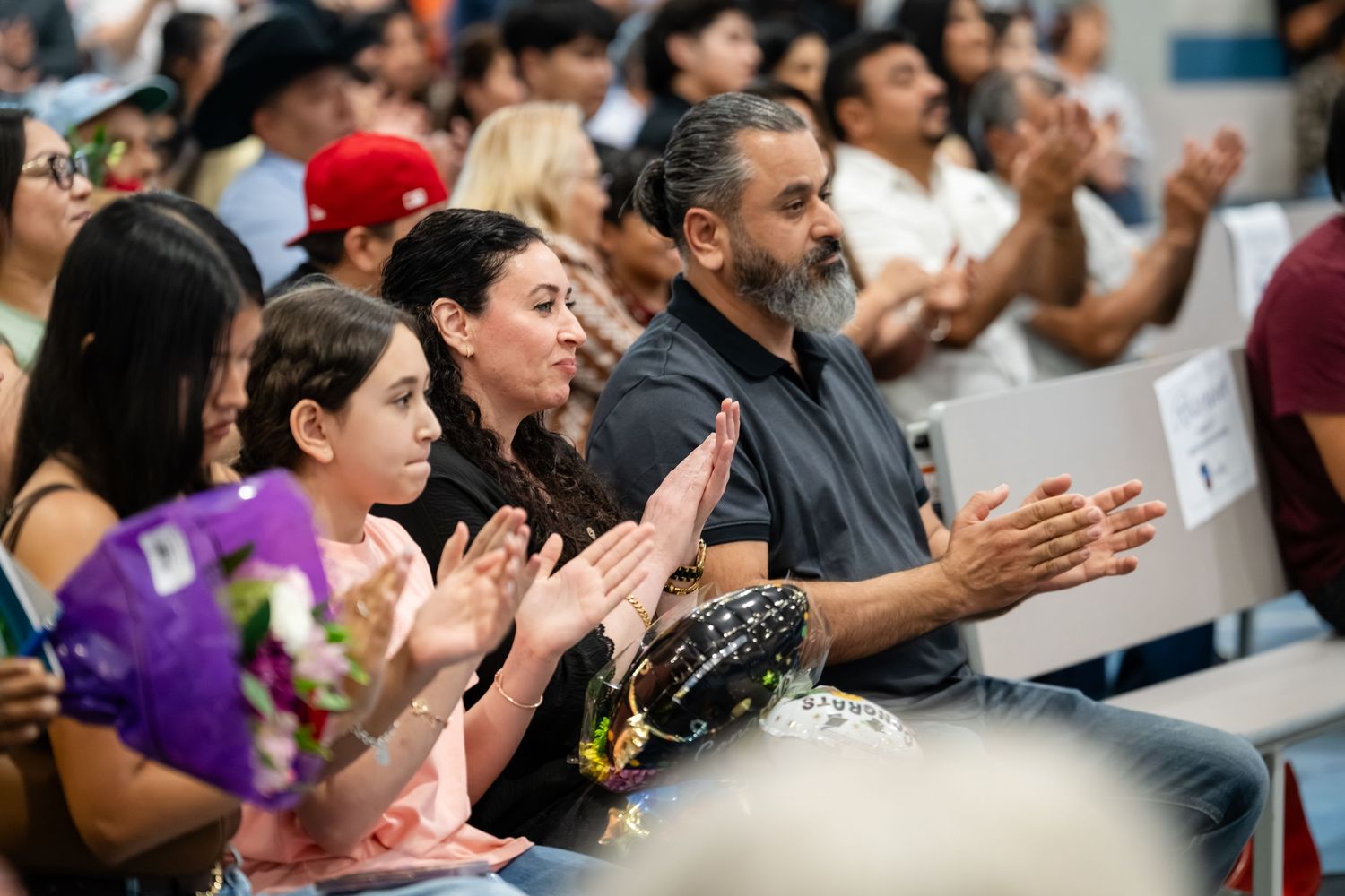 Diverse audience clapping and applauding at an indoor graduation or school ceremony event.