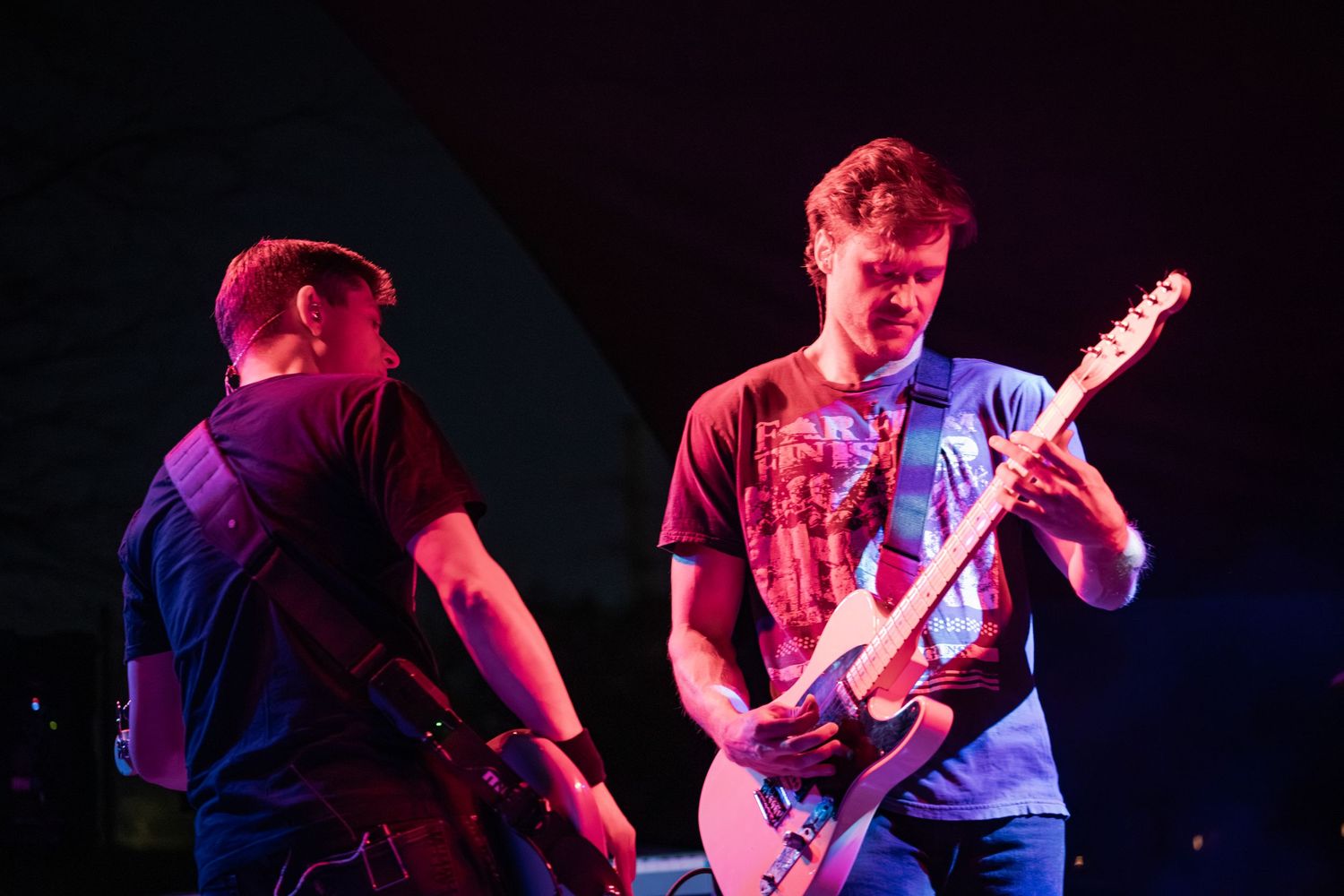 Two male guitarists performing on stage under colorful lights during a live rock concert.
