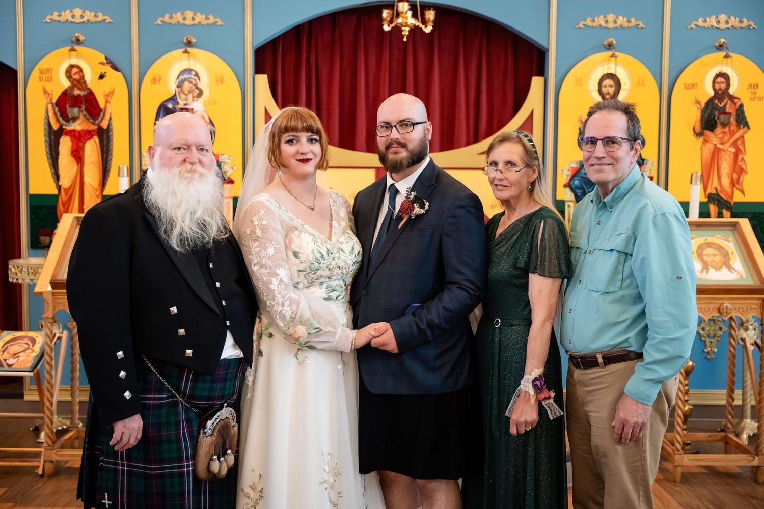 Wedding party members pose together in formal attire at an elegant indoor venue with ornate decor and religious icons.