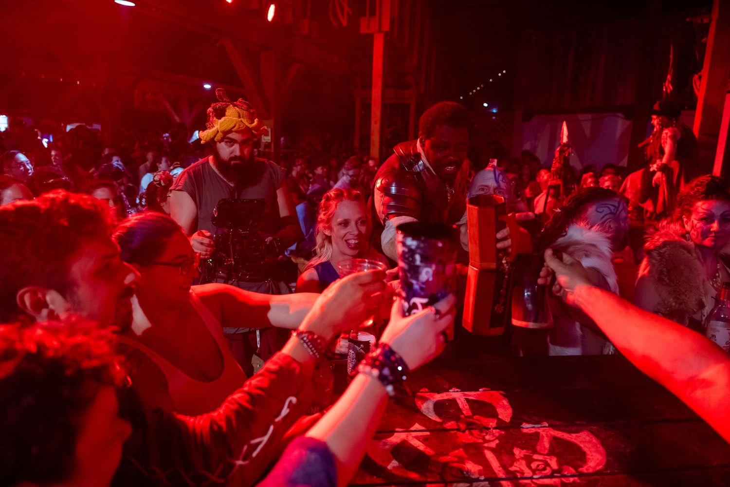 Concert crowd illuminated in red lighting dances and celebrates at a nightclub event during a live performance.