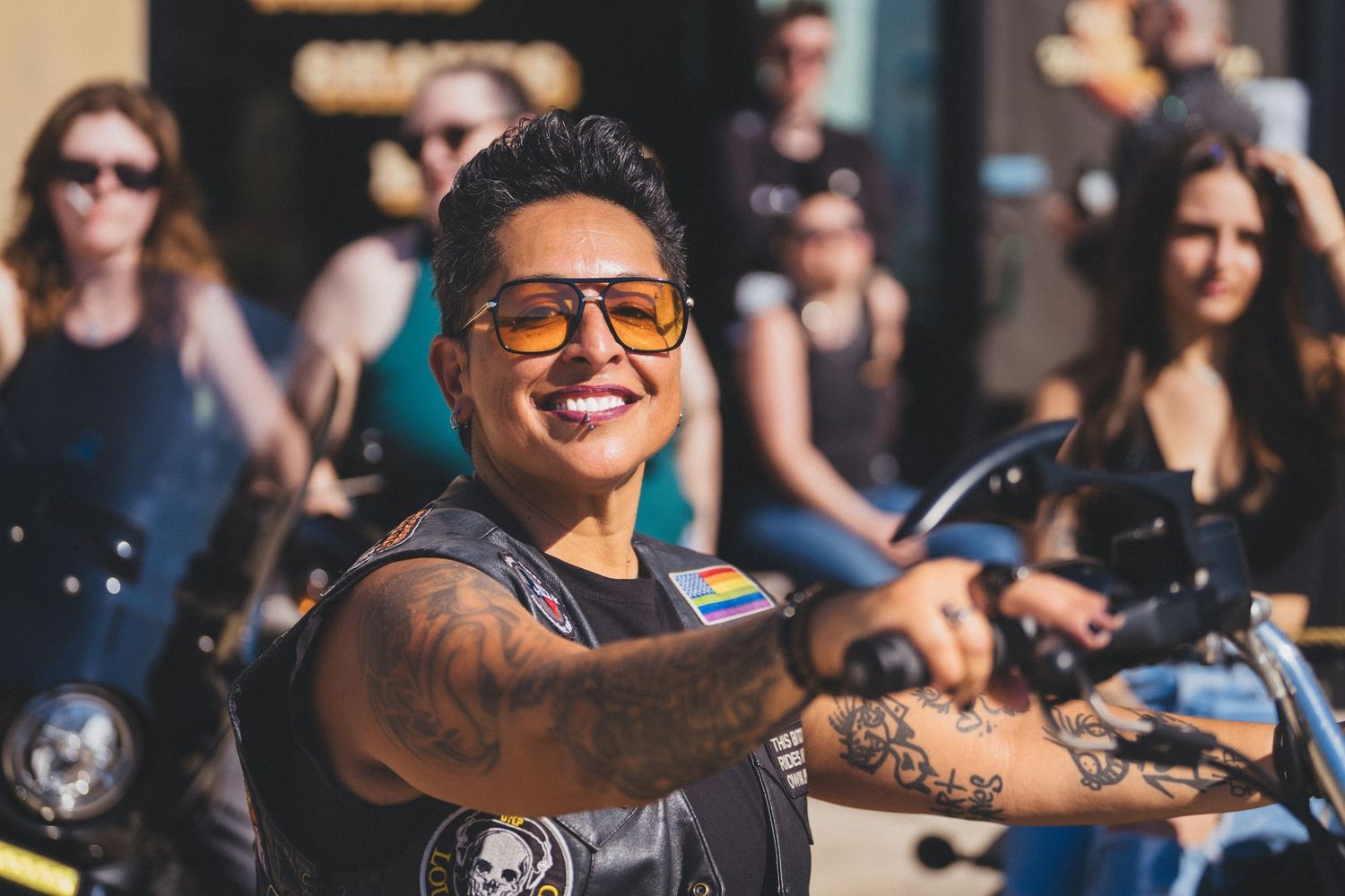 A group of motorcycle riders smile and enjoy a sunny day ride together on their bikes.