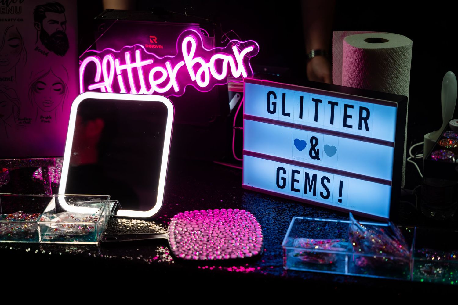 Pink neon glitter bar sign illuminates a light box display with 'Glitter & Gems' text and decorative elements.