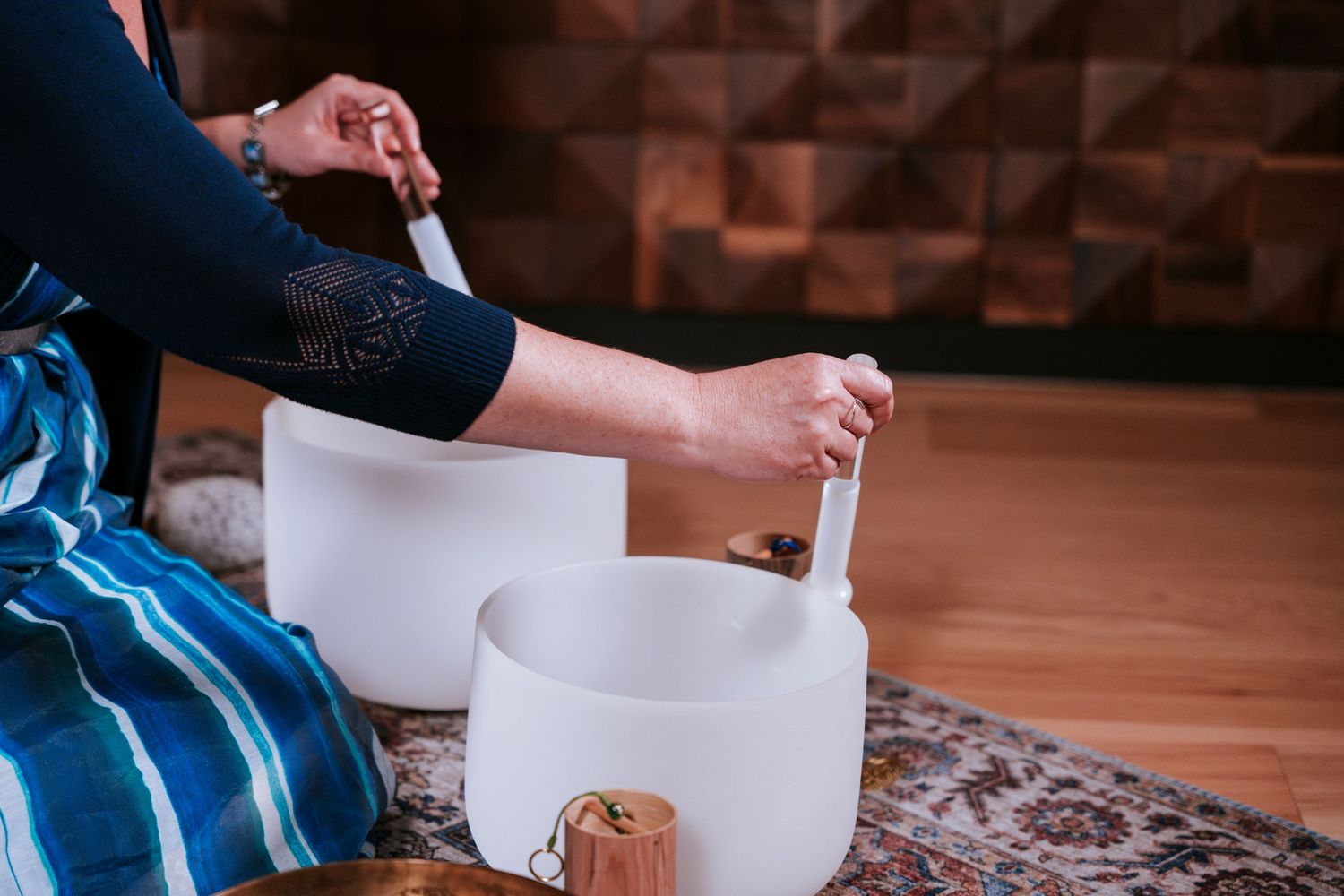 Someone practices sound healing with white quartz crystal singing bowls on a patterned rug.