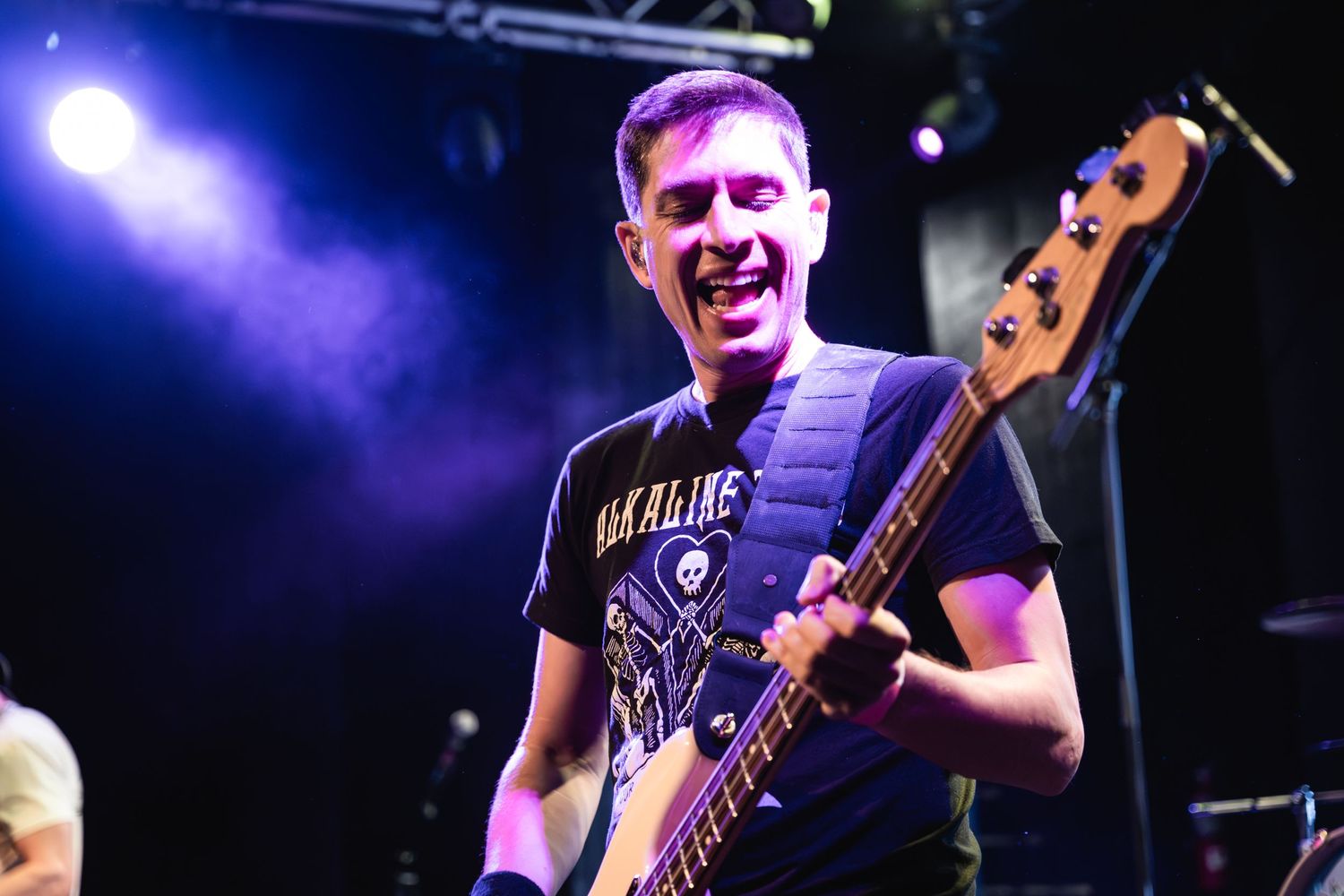 Bass player performs enthusiastically under dramatic purple stage lighting.