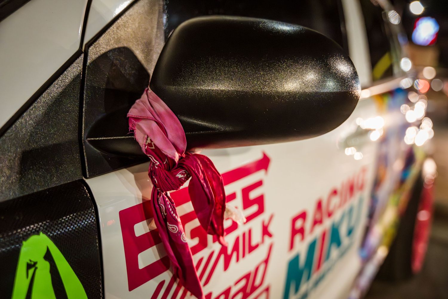 Close-up of red bandana tied to car mirror with promotional graphics visible in background.
