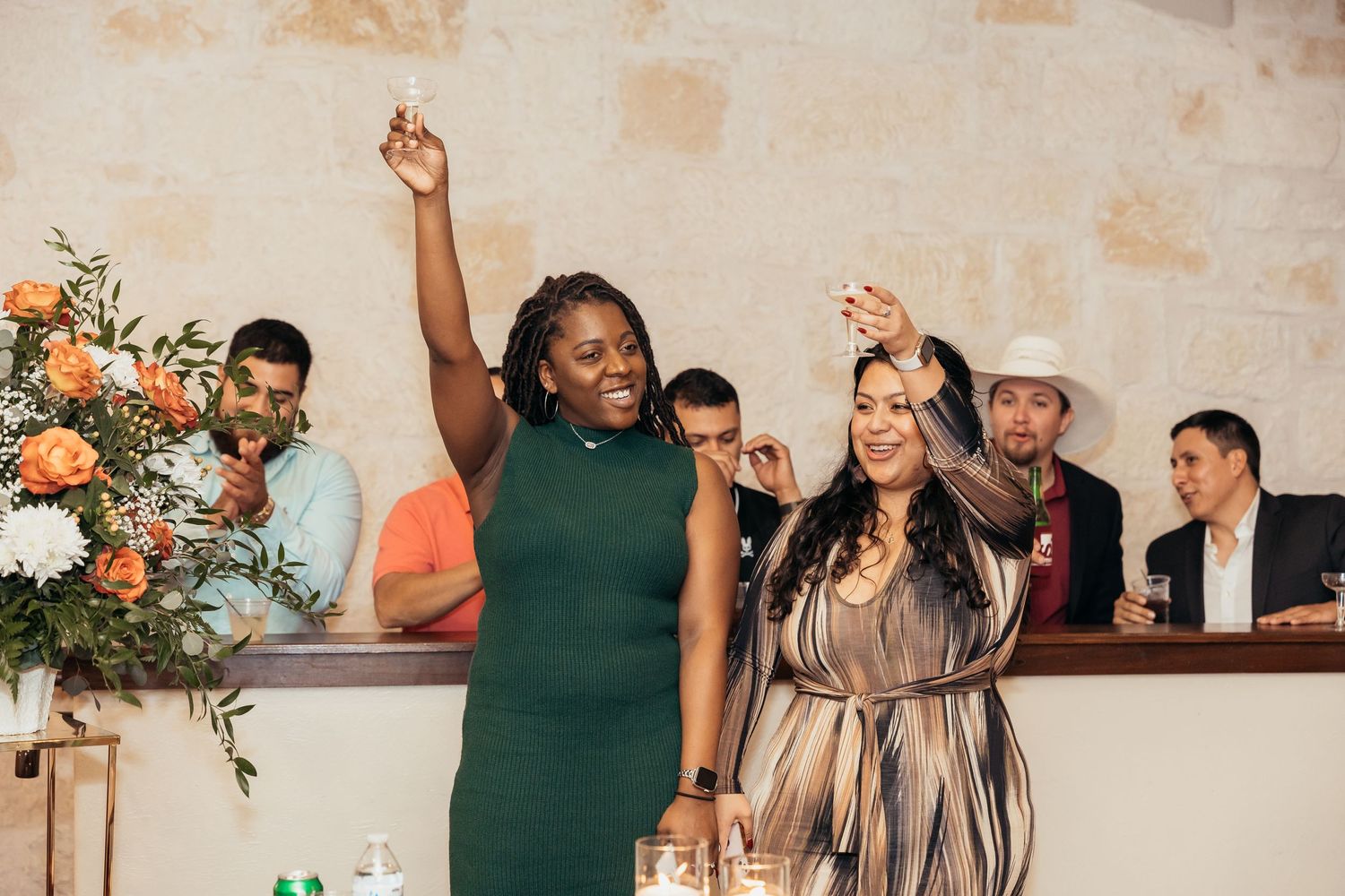 Wedding guests celebrate with raised arms next to floral arrangements.