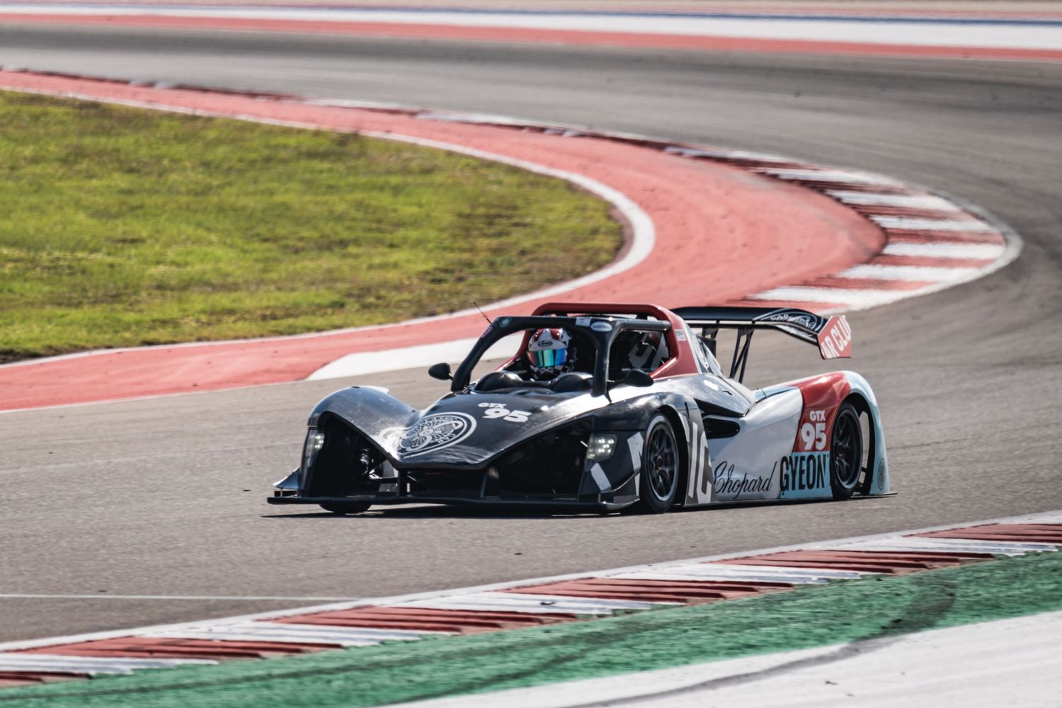 Black prototype race car takes a tight corner on a professional racing track.