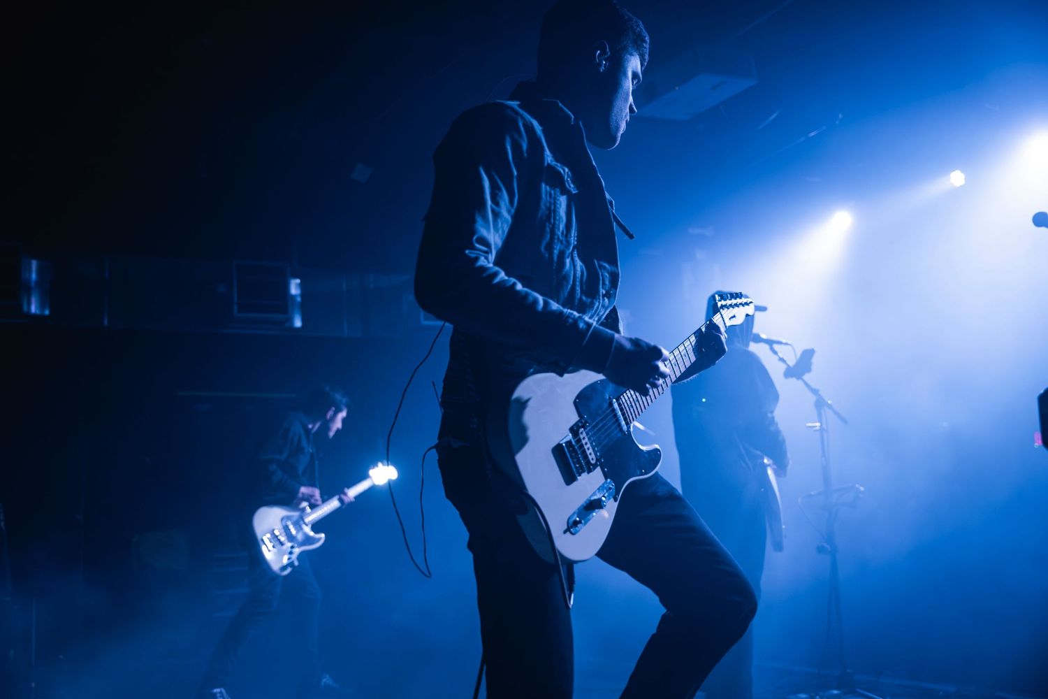 Musicians performing with guitars under blue stage lighting and fog effects.