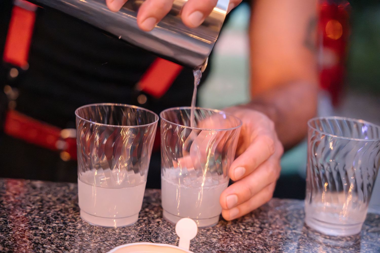Hands pouring drinks into crystal glasses on a dark granite bar surface.