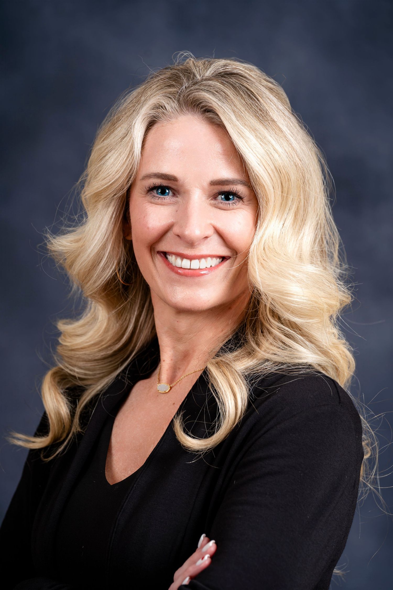 Professional portrait of woman in black blazer with blonde hair against dark backdrop.