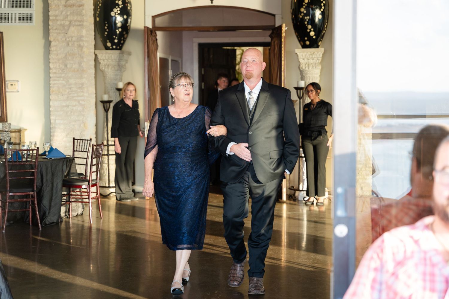 An elegant processional moment in a stone-walled venue with decorative wreaths.