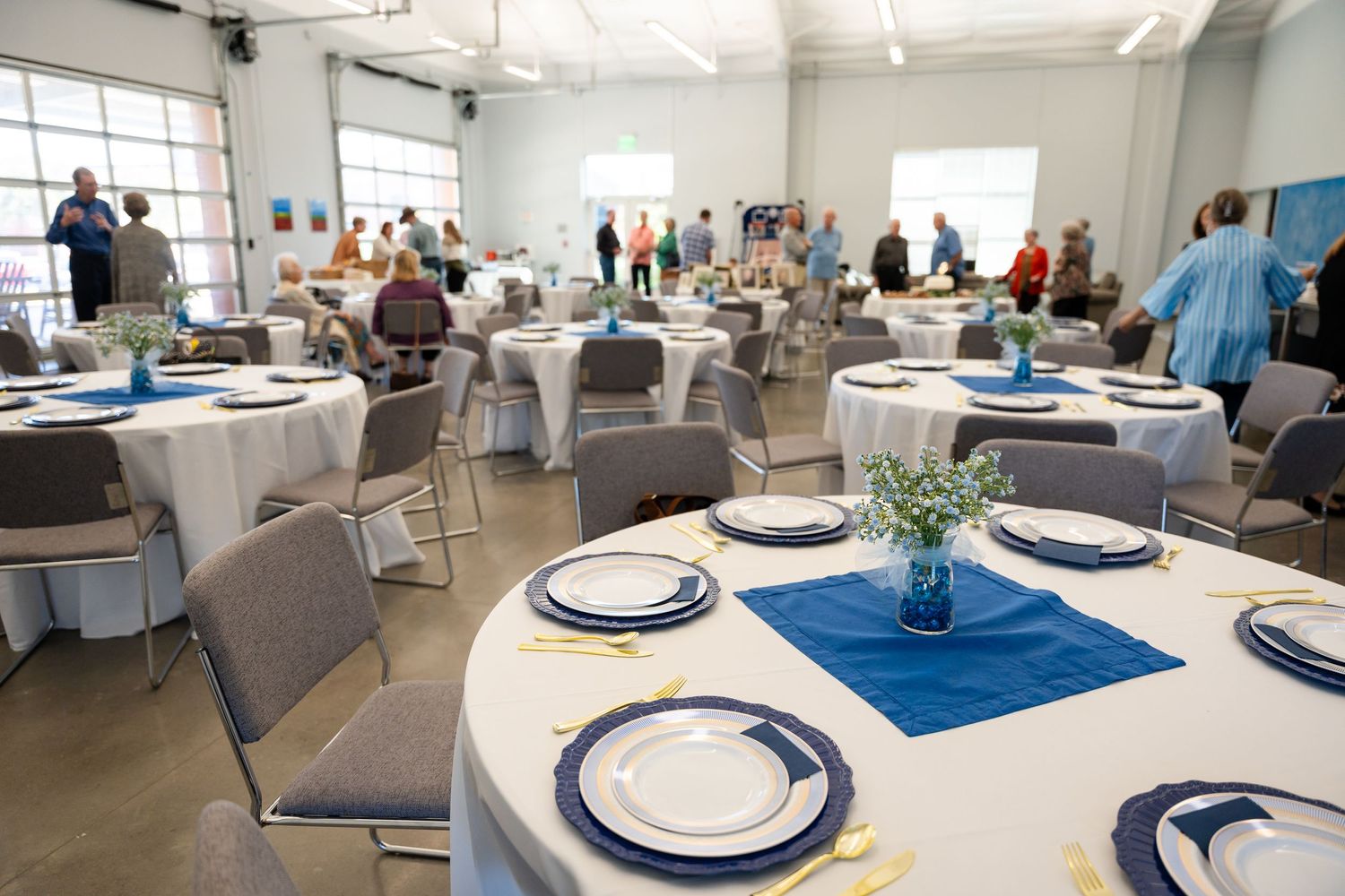 Event space setup with round tables, white tablecloths and blue accents.