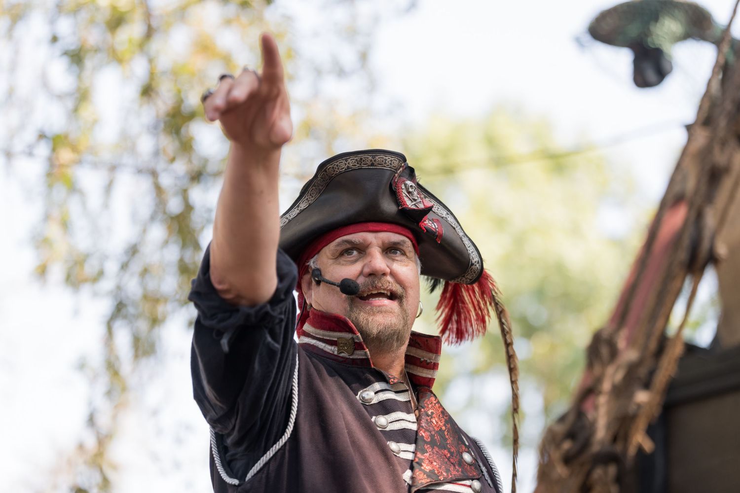 A pirate performer in tricorn hat gestures during a renaissance festival performance.