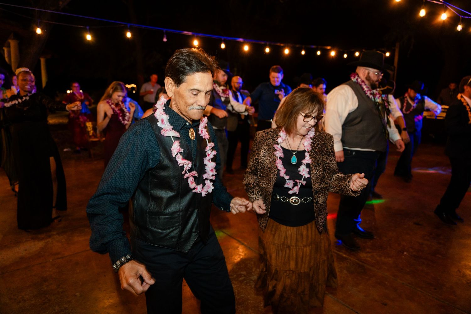 Dancers wearing Hawaiian leis move to the music at a nighttime indoor celebration.