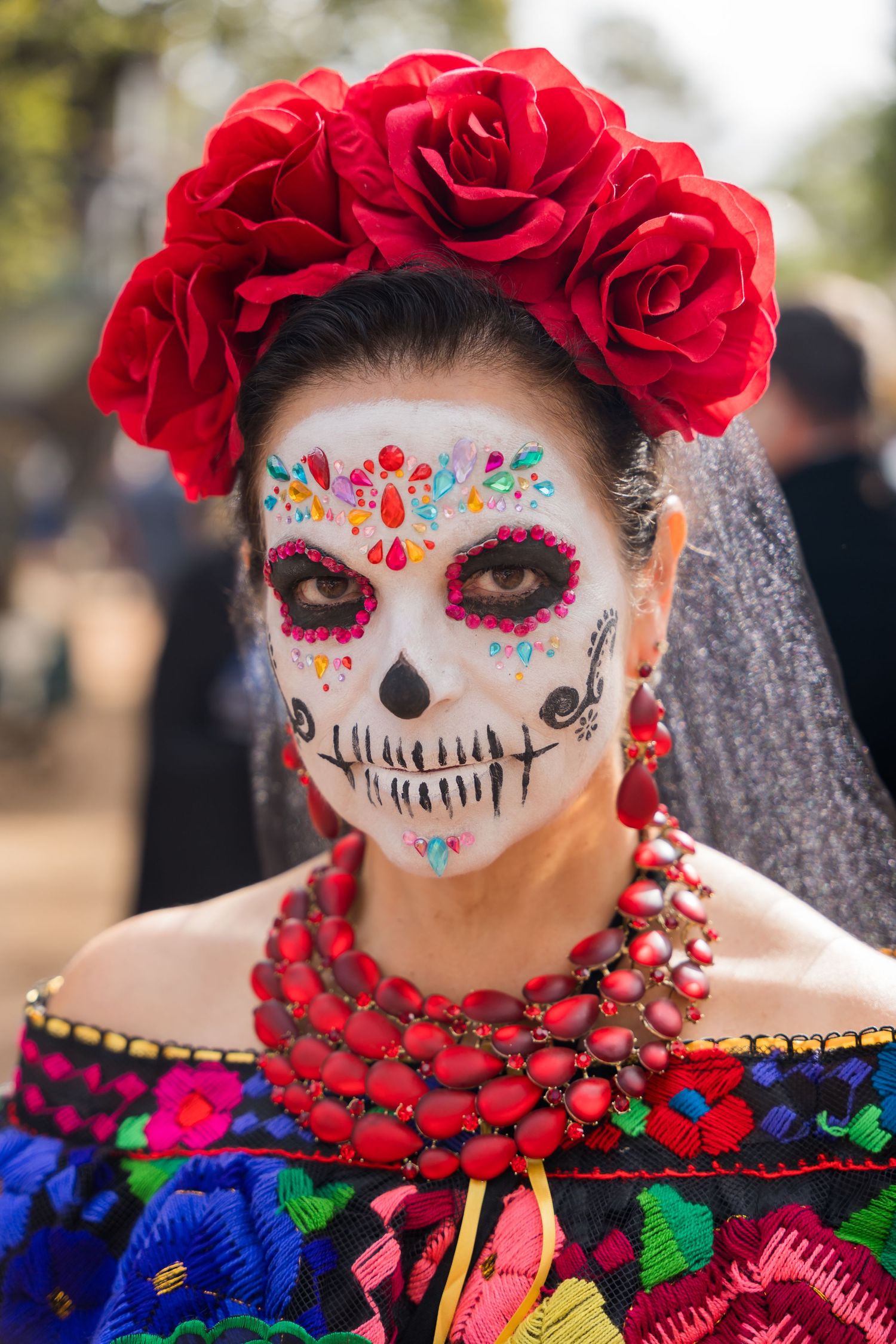 Traditional Day of the Dead makeup with red rose crown and colorful Mexican folk costume.