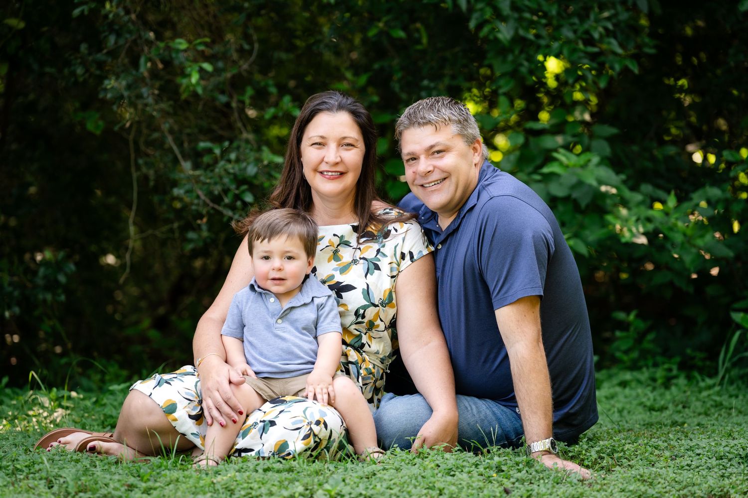 A casual family portrait in a garden setting with lush greenery background.