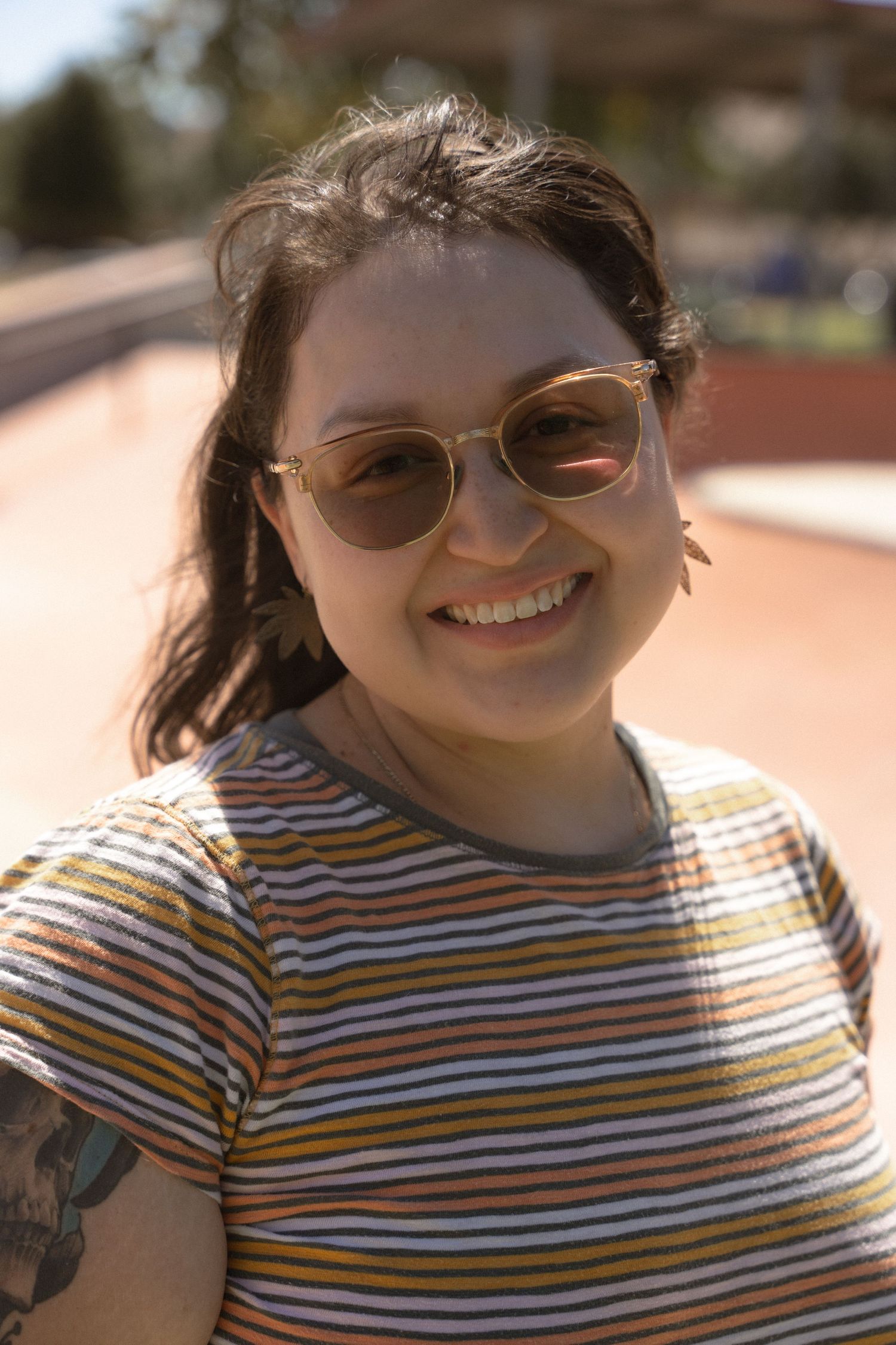 A person in a striped shirt and sunglasses smiles brightly in warm sunlight.