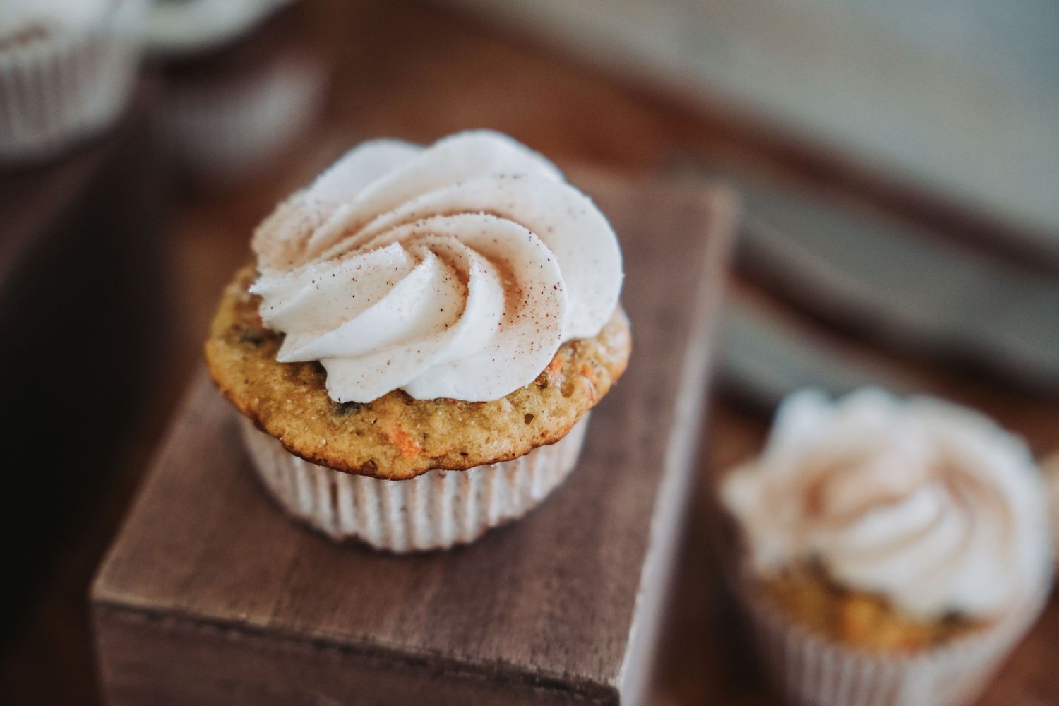 Close-up of vanilla frosted cupcake with swirled buttercream topping on wooden surface.
