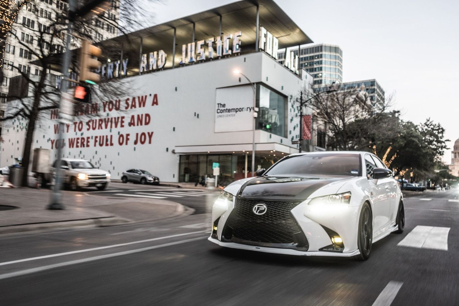 White Lexus sedan photographed in motion against urban theater backdrop.