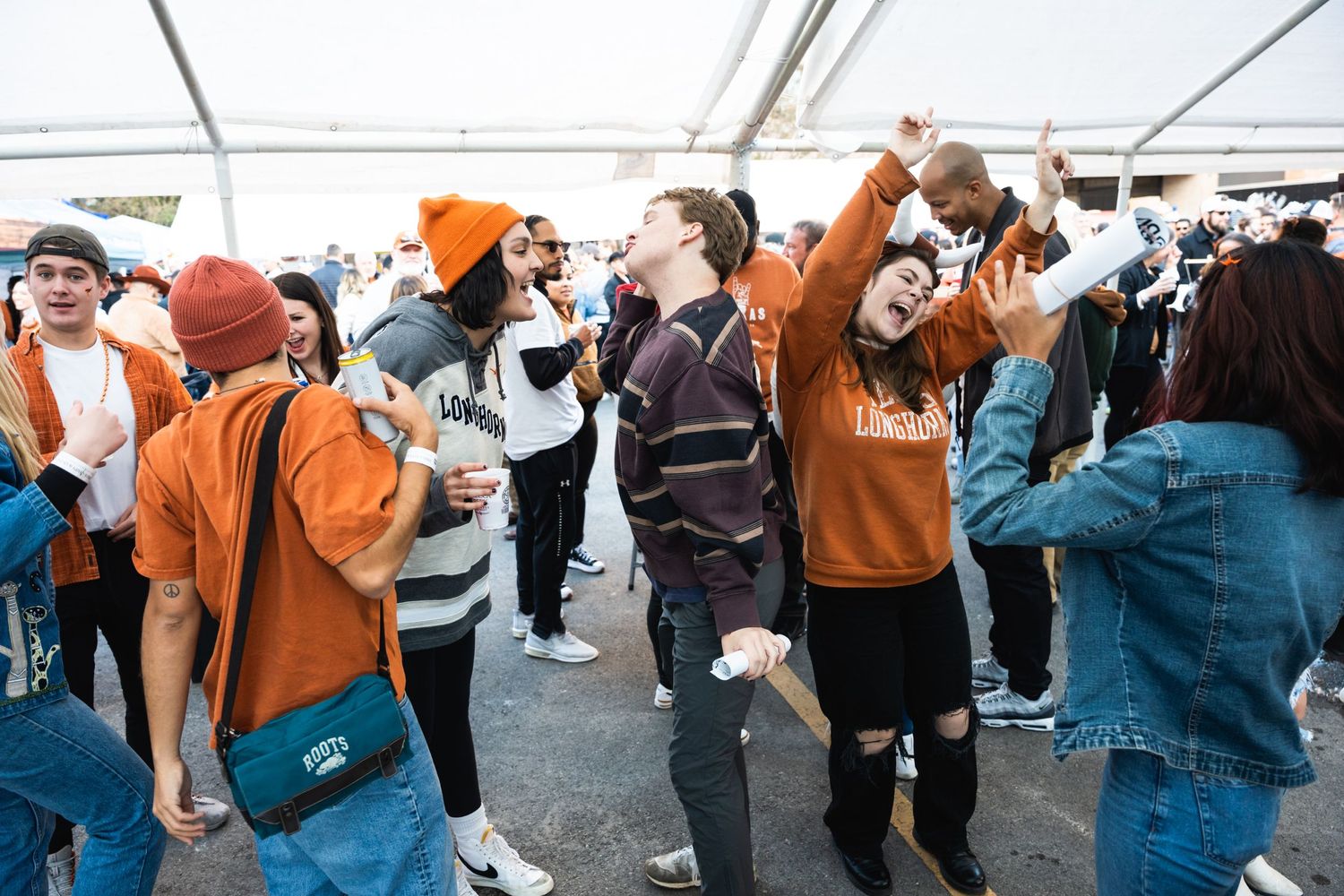 A crowd of people in orange and casual attire dancing and celebrating at an outdoor event.