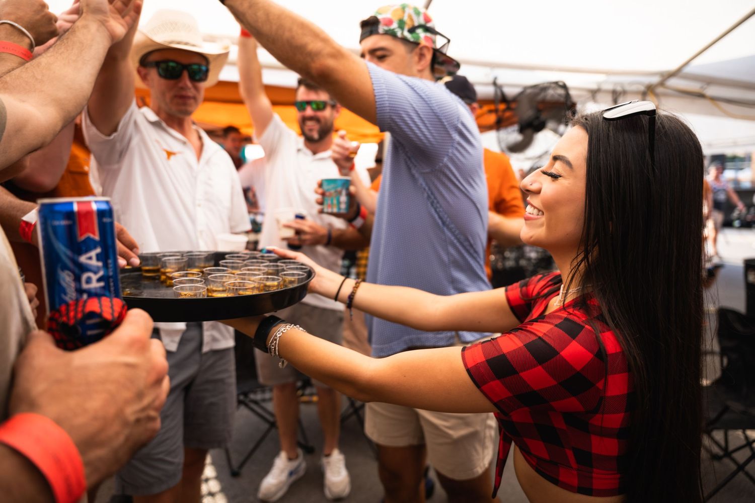 Partygoers celebrate at an outdoor event with drinks and food under a tent canopy.