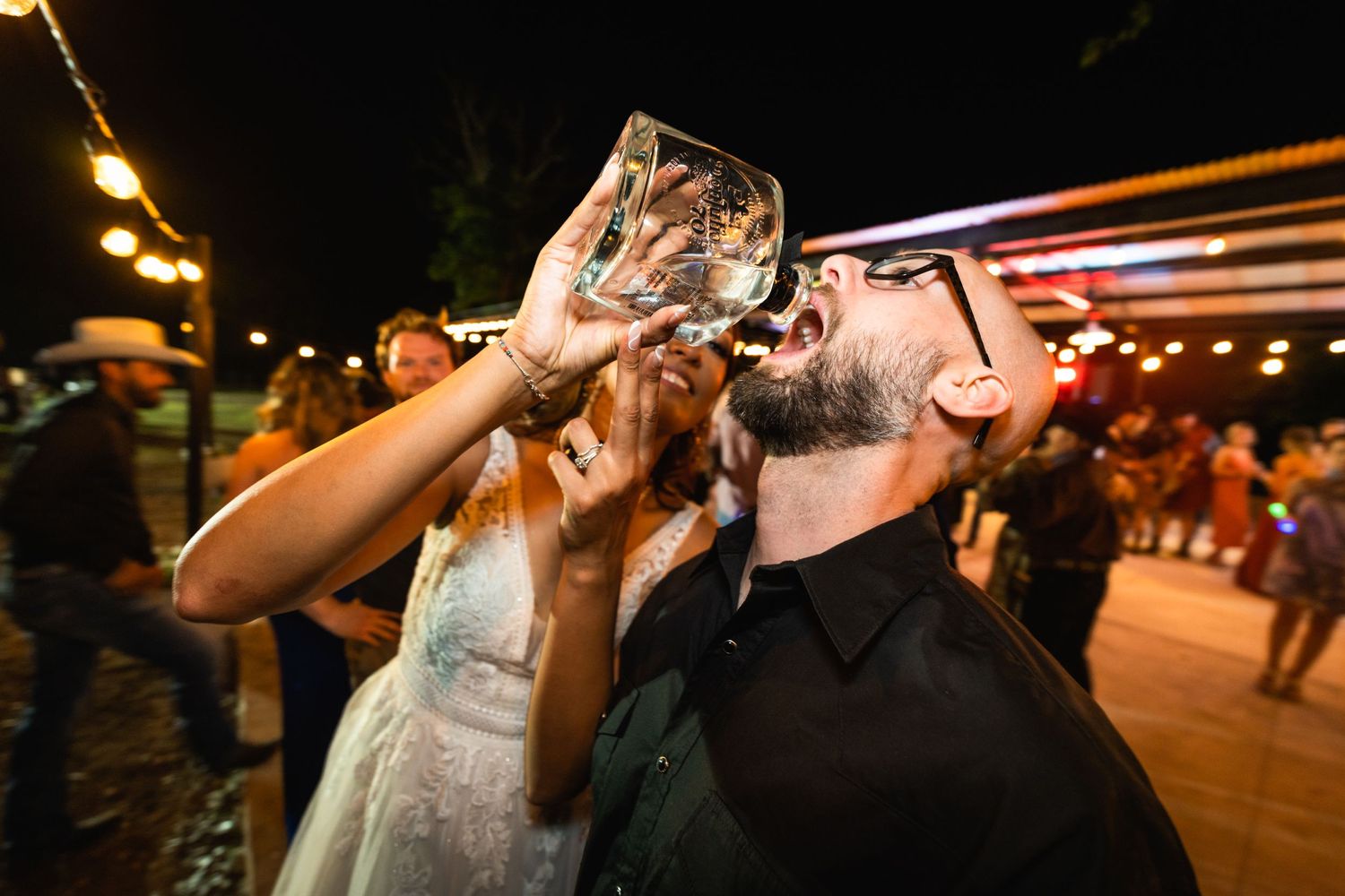 A couple taking celebratory drinks from glasses at an outdoor wedding reception.