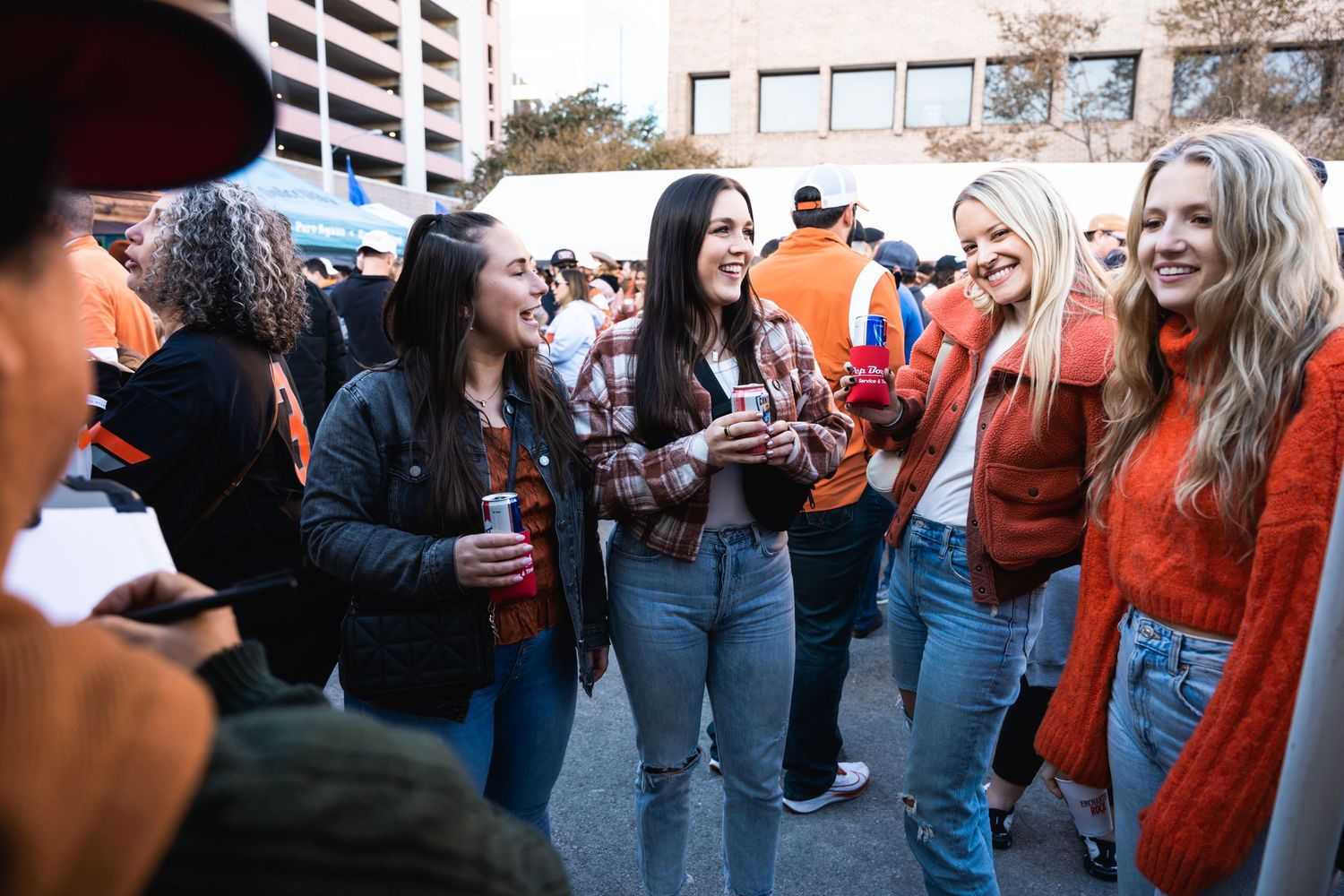 A group enjoying drinks and socializing at an outdoor gathering wearing orange fan gear.