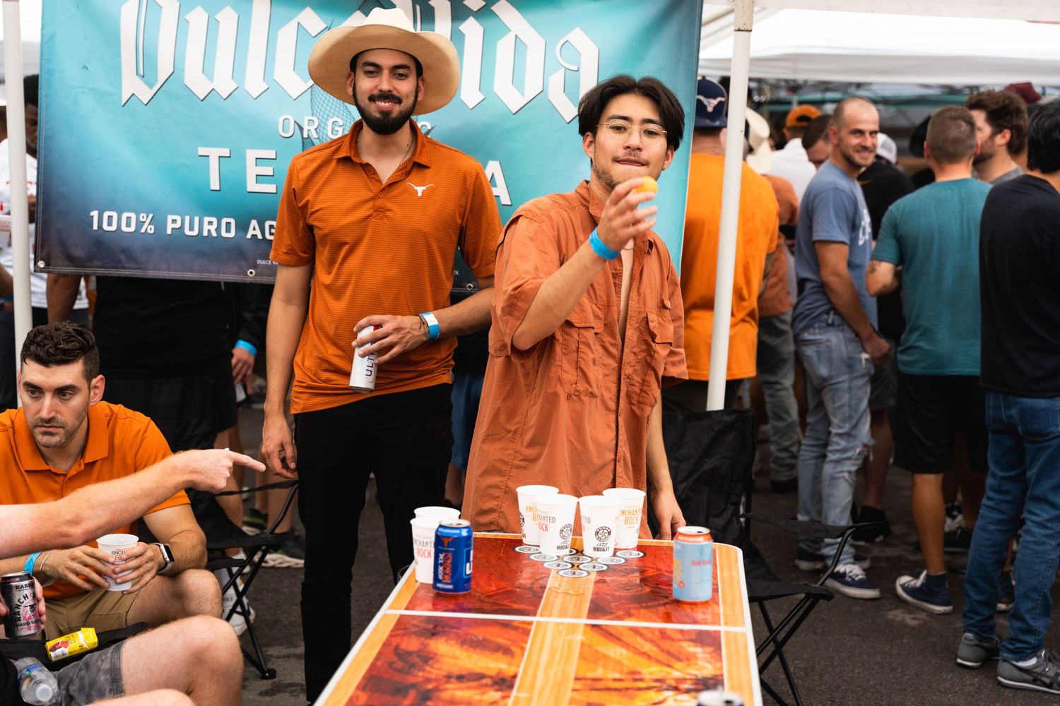 Two people in orange outfits serving drinks at an outdoor vendor booth with a blue banner.