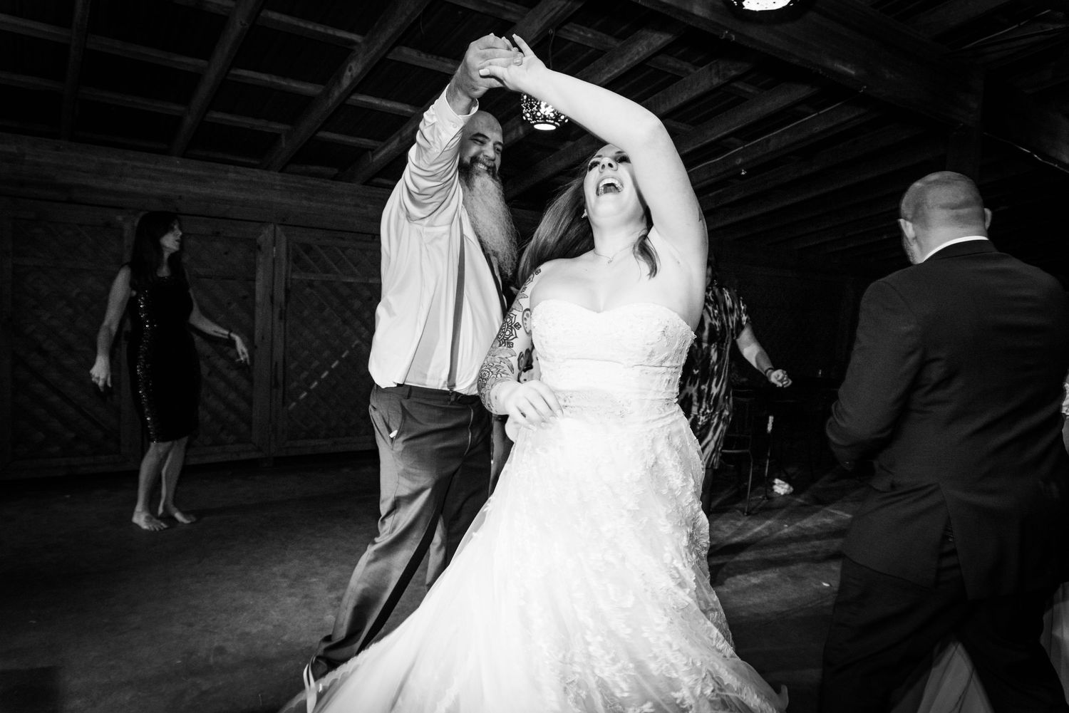 A couple dances together at a wedding reception in a dimly lit venue, with the bride wearing a white gown.