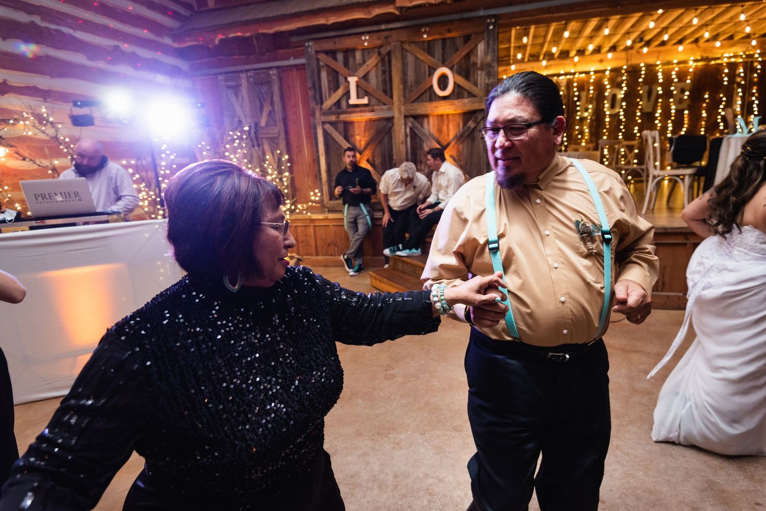 People dancing joyfully at a rustic barn wedding reception with twinkling lights in the background.