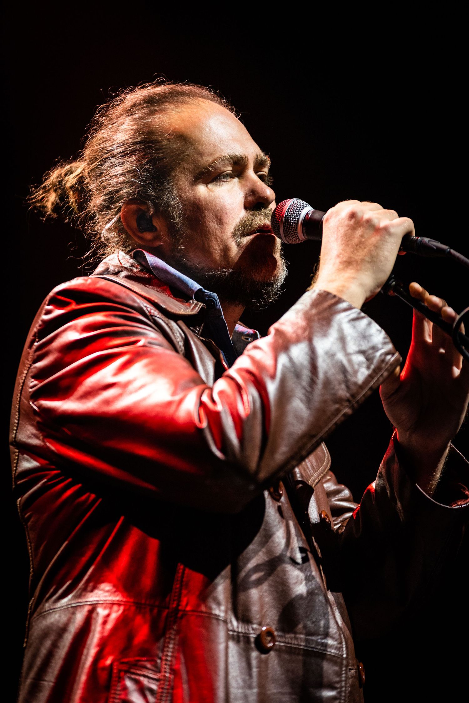 Close-up concert shot of performer singing intensely into microphone under red stage lights.