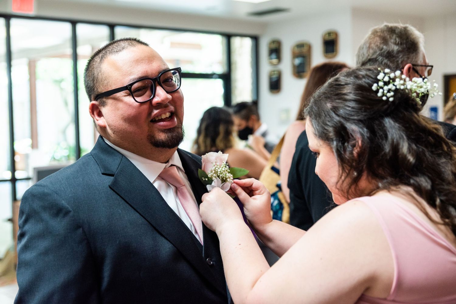 A pink-tied groomsman gets his boutonniere pinned on during wedding preparations.