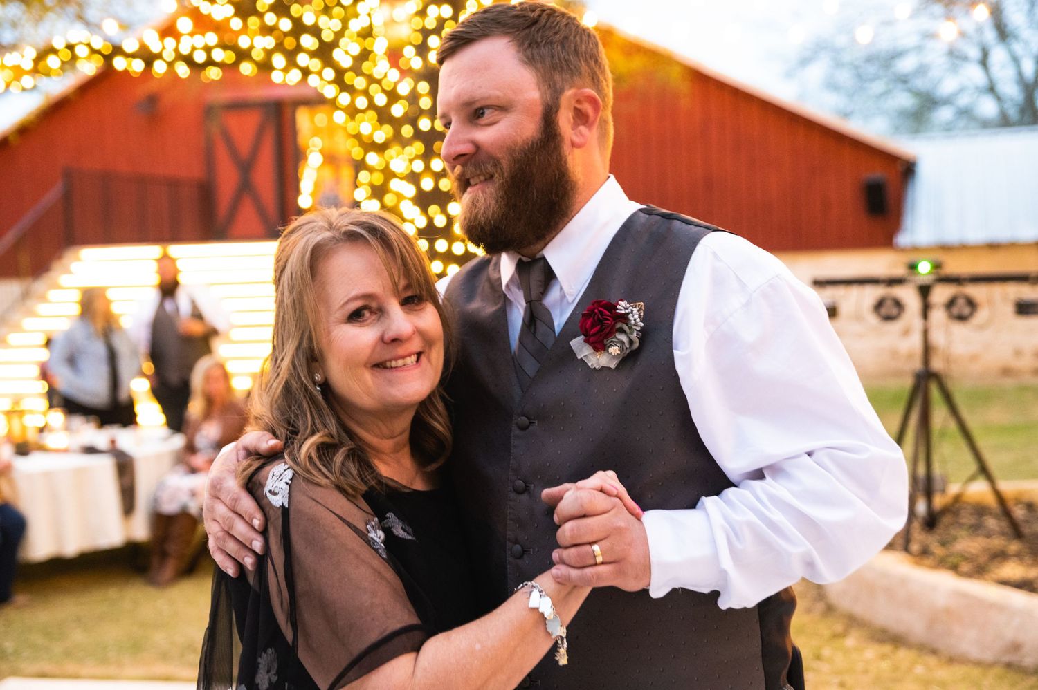 Couple poses near illuminated red barn during evening wedding reception.