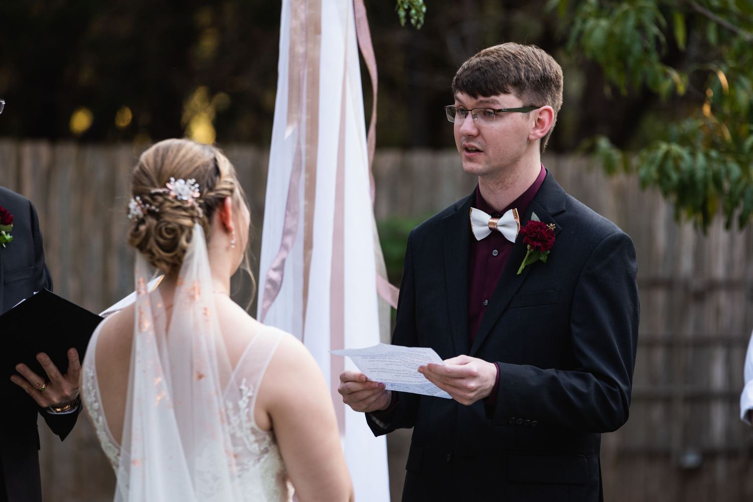An outdoor wedding ceremony with exchanging of vows against a backdrop of autumn foliage.