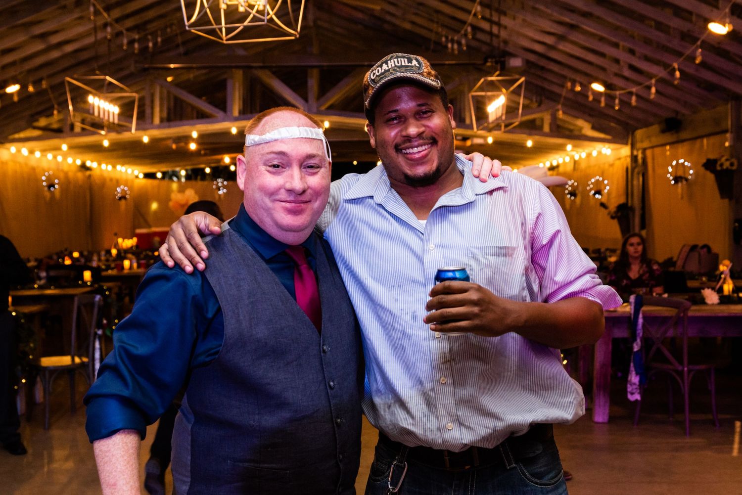 Two guests posing together at a wedding reception with string lights decorating the ceiling.
