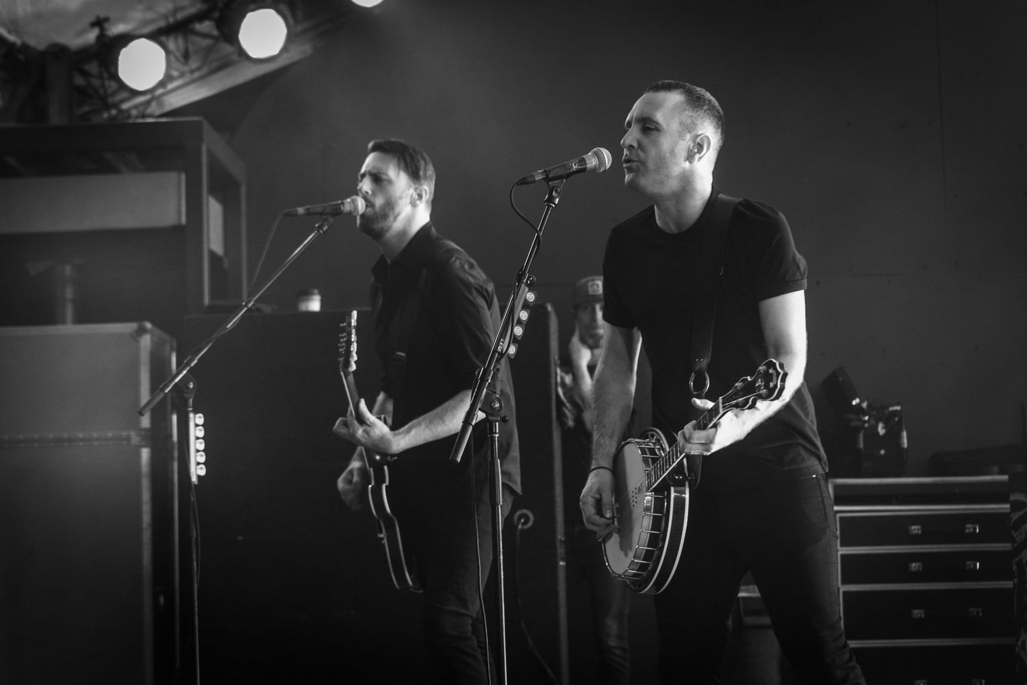 Two musicians perform with guitars in black and white under dramatic stage lighting.
