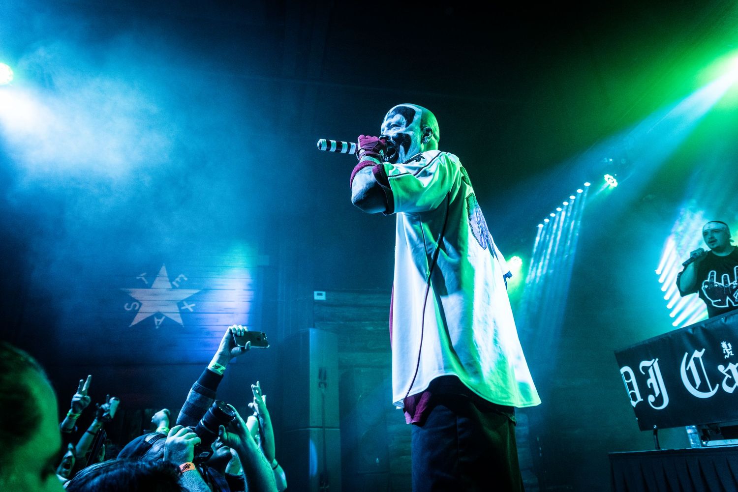 Performer in white clothing on stage with blue and green lighting effects.
