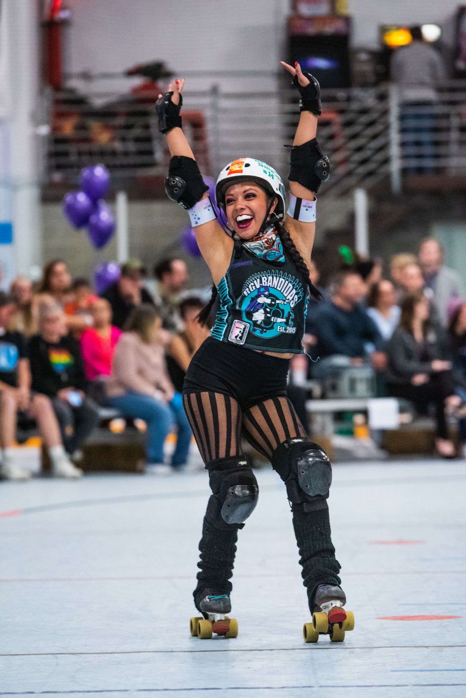 Roller derby skater celebrates with arms raised while skating in blue uniform.