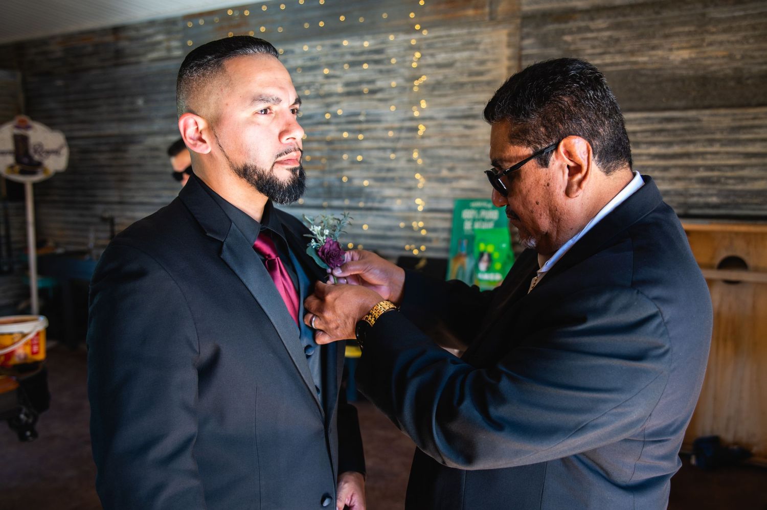 Someone adjusts another's formal attire in a dimly lit room with string lights.